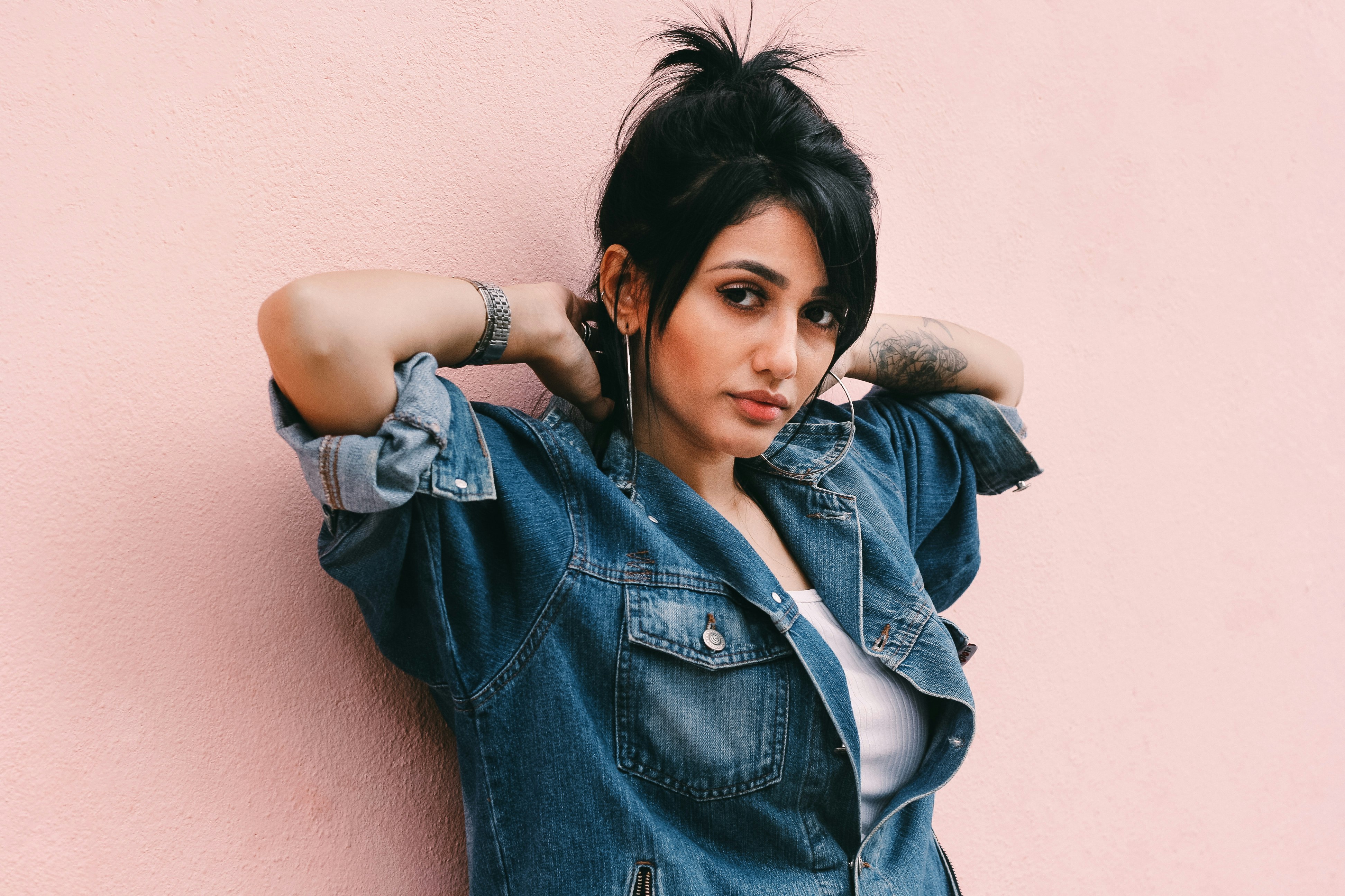 Woman wearing a denim wall leaning against a millennial pink wall